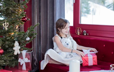 Criança abre presente perto de árvore de natal