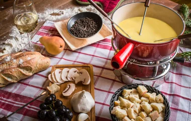 Fundue de queijo, cogumelos, pão rústico e caviar são dispostos em uma mesa com toalha quadriculada vermelha e branca.