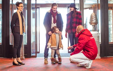 G.O. conversa com criança pequena com a supervisão dos pais na entrada do resort de neve