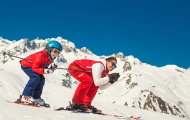 Pai e filho se agacham performando manobra de esqui na neve