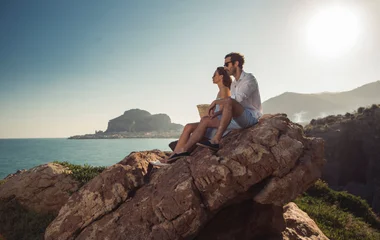 Pareja sentada en lo alto de una roca con vistas al mar.