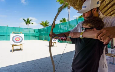 Instrutor ensinando crianças a atirar com arco e flecha.