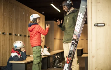 Um pai e seus dois filhos dentro da Ski Pro Room, espaço de custo adicional que disponibiliza armários para os equipamentos de neve.
