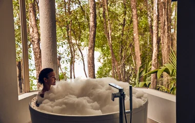 Mujer en bañera, con paisaje forestal al fondo.
