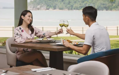 Una pareja, un hombre y una mujer, brindando con copas de vino blanco.