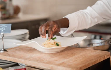Mão do chef finalizando prato com massa italiana.