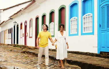 casal de mãos dadas em ruas de paralelepípedos em frente a casas coloridas