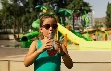 Menina bebendo suco em frente ao parque aquático.