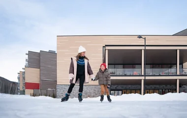 Adulto e uma criança de mãos dadas patinando no gelo.