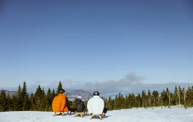 Três amigos sentados em trenós com vista para os Alpes.