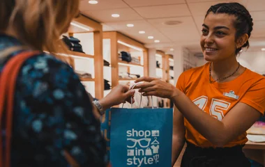 Uma GO entregando uma sacola de souveniers para uma GM em uma Boutique de um resort Club Med