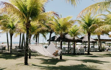 Uma pessoa deitada em uma rede no meio de uma praia do Club Med Trancoso no meio de palmeiras.