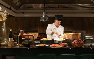 Um chefe preparando um prato em uma mesa farta.