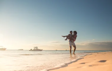 Homem carregando a mulher no colo na praia.