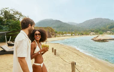 Casal em pé na praia tomando água de coco