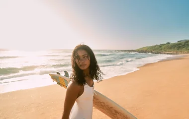 Mulher na praia com prancha na mão.