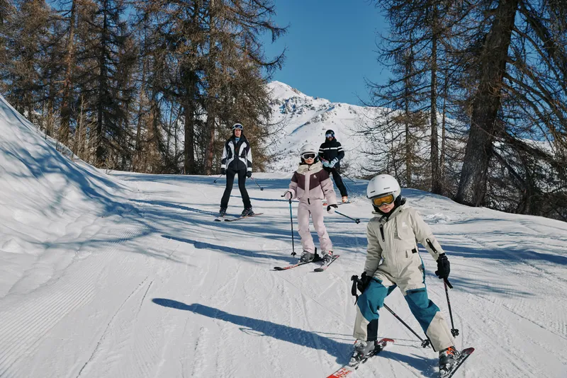 Familia esquiando en pista entre abetos
