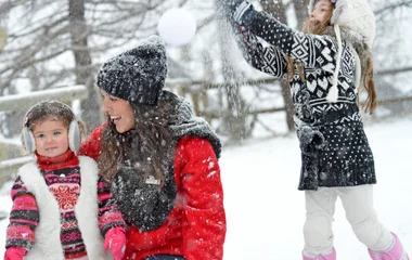 Close de bebê agasalhado com casaco e gorro azul com sua mãe agachada segurando-o. Ao fundo montanhas nevadas.