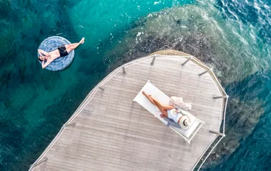 mulher deitada em esteira em frente ao mar com homem em boia