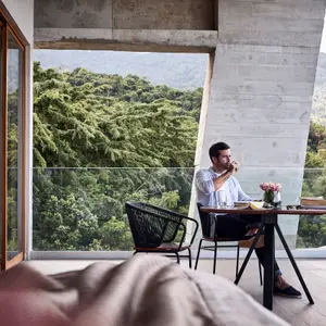 Mulher olhando o marido tomar café na varanda da suíte.