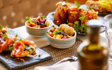 Duas tigelas de salada de frutas ao lado de um prato com acarajé e outro de entradas com salmão fresco.