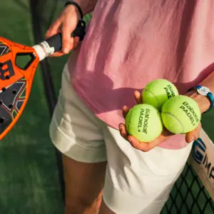 Pessoa com raquete e bolas de tênis na mão, pronta para treinar