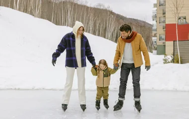 pais segurando as mãos da filha enquanto patinam no gelo