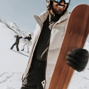 Homem com prancha de snowboard na mão e ao fundo montanhas cobertas de neve