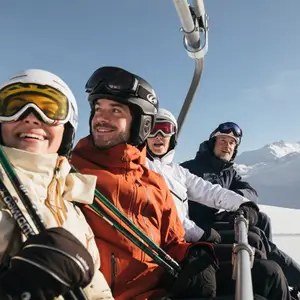 grupo de amigos sorrindo em montanha com neve, segurando equipamentos de esqui