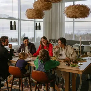 Família sentada à mesa do restaurante no almoço com as montanhas de neve ao fundo das grandes janelas