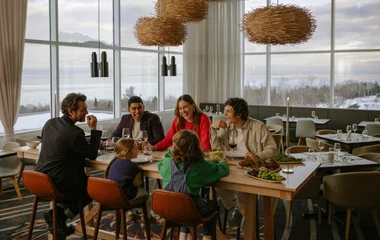 Um homem e duas mulheres sentados a mesa à luz de velas brindam com uma taça de vinho tinto