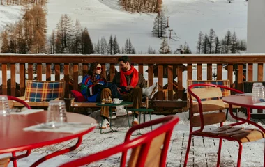 Pareja en el área exterior de Pragelato disfrutando de unos snacks durante el día, rodeados de nieve.