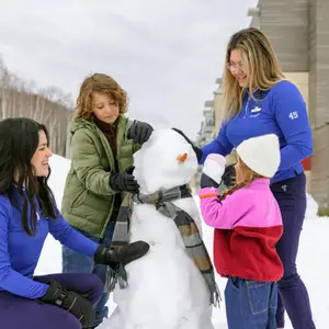 Duas crianças e duas mulheres fazendo um boneco de neve.