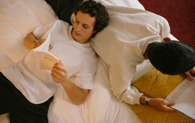 Dois homens lendo no quarto deitados na cama