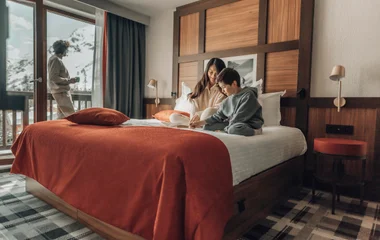 Mãe e filho na cama, e pai na varanda da suíte.