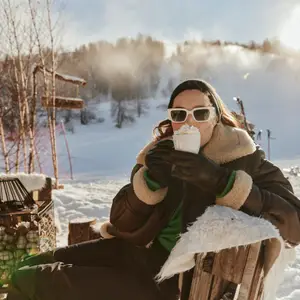 Mulher sentada em área aberta com neve, tomando chocolate quente com chantilly