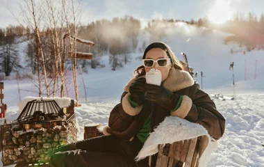 Mujer sentada en un área al aire libre con nieve, tomando chocolate caliente con crema chantilly.