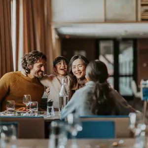Casal de homem e mulher na varanda do resort com a montanha nevada e os chalés ao fundo.