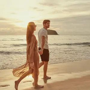 Casal de homem e mulher caminhando na areia da praia no por do sol