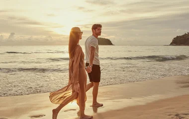 Pareja de hombre y mujer caminando por la arena de la playa al atardecer.