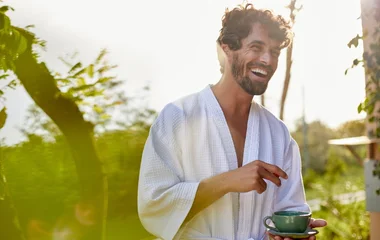 Homem de roupão sorrindo enquanto segura uma xícara de chá.