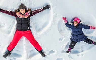 Mãe e filha fazendo anjos de neve.