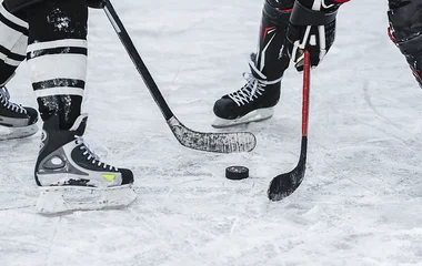 Primer plano de dos palos de hockey en el suelo sostenidos por dos jugadores.