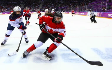 Partido de hockey y dos jugadores al frente, uno de ellos vistiendo un uniforme canadiense.