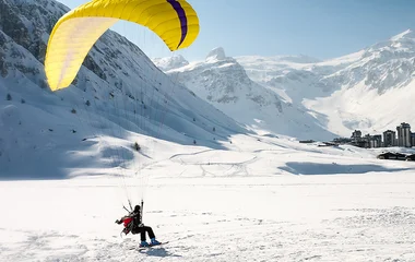 Pessoa saltando de parapente na neve.