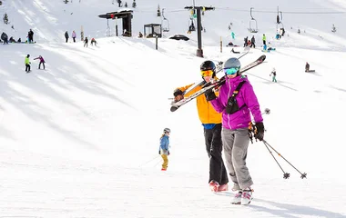 Casal com roupa e equipamento de esqui andando na neve.