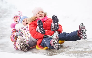 Três crianças descendo a neve no trenó.