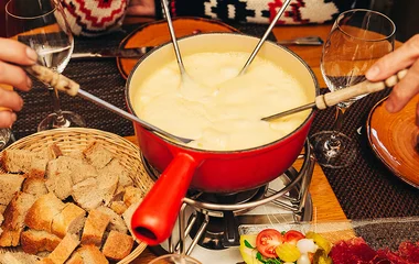 Fondue de queijo com acompanhamentos ao redor.