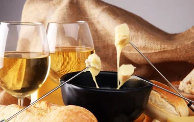 Fondue de queijo ao lado de duas taças de vinho.