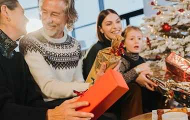 Familiares com criança em clima de Natal segurando presentes com uma árvore de natal branca ao fundo